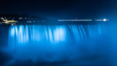 Blurred streams of Niagara Falls, illuminated in blue in the evening. Canada. One of the world's main attractions. Close-up. clipart