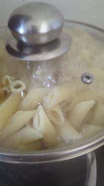 Penne makarna yakın plan kapalı şeffaf kapağın altında bir tencerede kaynatılır. Yemek pişirme.
