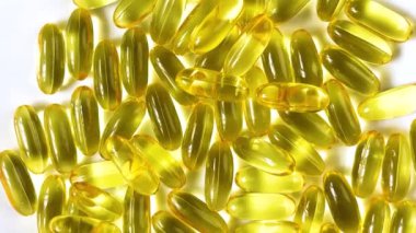 Yellow transparent capsules with liquid Omega 3 on a white background. The concept of maintaining and improving health, Fish oil is an essential supplement for wellness. Slow motion. Close up.