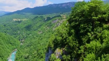 Turist, Tara Nehri Kanyonu ya da yüksek dağlar arasındaki Tara Nehri Vadisi üzerinde bir halatla kayar. Kanyon Avrupa 'daki en büyük ve en derin kanyondur. Durdevica Tara Köprüsü 'nden görüntü. Karadağ.
