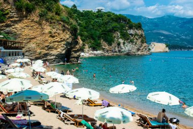 Morgen plajı, Karadağ - 4 Temmuz 2021: Budva yakınlarındaki kumlu plajda güneş pansiyonları ve şemsiyeler. Yaz güneşli manzarası.