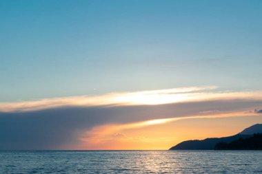 Denizin üzerinde güzel bir gün batımı. Batan güneşin turuncu ışıkları gökyüzünü ve süslü bulutları aydınlatıyor..