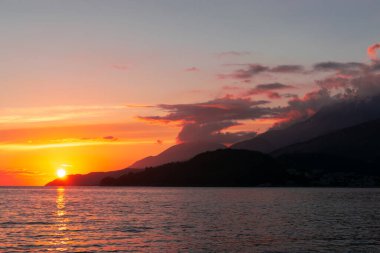 Denizin üstünde muhteşem bir gün batımı. Batan güneşin turuncu pembe ışınları gökyüzünü ve süslü bulutları aydınlatıyor..