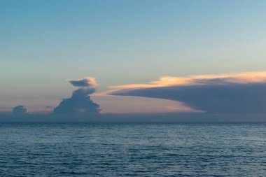 Denizin üzerinde güzel bir gün batımı. Batan güneşin turuncu pembe ışınları gökyüzünü ve süslü bulutları aydınlatıyor..