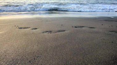 Bir adamın ayakları kumsaldaki siyah, ıslak volkanik kumda yürür. Kanarya Adaları 'nın en ilgi çekici sahillerinden biri. Kapatın. Playa de la Arena, Tenerife, İspanya. Atlantik Okyanusu.