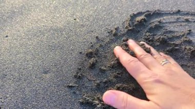 Kadının eli Atlantik Okyanusu 'nun gelen dalgalarından ıslanmış siyah volkanik kuma dokunuyor. Kanarya Adaları 'nın en ilgi çekici sahillerinden biri. Kapatın. Playa de la Arena, Tenerife, İspanya.