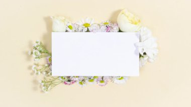 Beyaz papatya tomurcukları, kasımpatı ve papatya çiçekleri dikdörtgen beyaz bir kağıt parçasının yanında belirir. Metin ya da tasarım için şablon. Bej renkli pastel arka plan. Bayram kartı. Hareketi durdur.