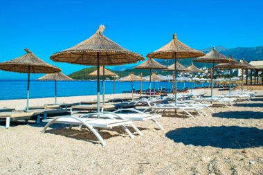 Saman plajı şemsiyeleri ve temiz kum ve çakıl taşı plajındaki rahat güneş şezlongları. Himare. Arnavutluk. İyon Denizi. Tatil deniz konsepti. Yaz güneşli deniz manzarası.