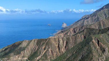 Yeşil dağlar ve uçurumlardan oluşan güzel bir manzara. Mirador Bailadero 'nun sahile ve Atlantik Okyanusu' na bakış açısı. Bulutlu mavi güneşli gökyüzü. Anaga Kırsal Parkı, Tenerife. Kanarya Adaları, İspanya.