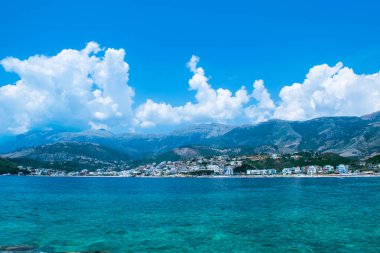 Himare 'nin dağların eteğindeki çakıl taşlı sahil kasabasının güzel yaz bulutları manzarası. Adriyatik denizleri. Arnavutluk. Yaz tatili ve rahatlama kavramı.