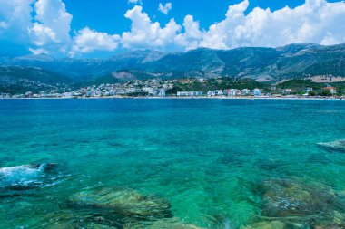 Himare 'nin dağların eteğindeki çakıl taşlı sahil kasabasının güzel yaz bulutları manzarası. Adriyatik denizleri. Arnavutluk. Yaz tatili ve rahatlama kavramı.