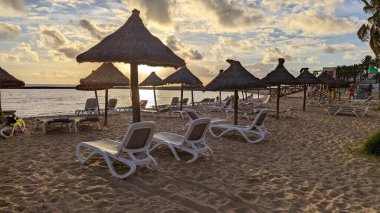 Playa de las Americas, Tenerife, İspanya - 7 Ocak 2025: Güneşin batışında palmiye ağaçları, güneş panjurları ve şemsiyeli güzel geniş kumlu plaj. Atlantik Okyanusu.