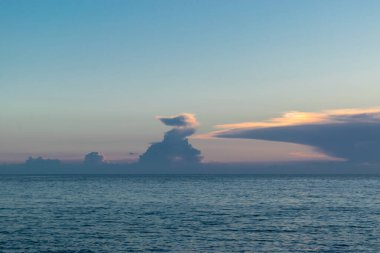 Denizin üzerinde güzel bir gün batımı. Batan güneşin turuncu pembe ışınları gökyüzünü ve süslü bulutları aydınlatıyor..