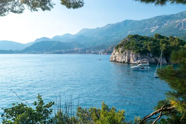 Karadağ kıyılarının güzel manzarası. Ufuktaki dağ sıraları ve sahildeki yeşil çam ağaçları. Mavi yaz güneşli manzarası. Budva yakınlarındaki Adriyatik kıyıları.