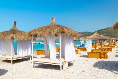 Borsh Beach, Arnavutluk - 14 Temmuz 202: Açık mavi suyla bir çakıl taşı plajında konforlu yataklar. Bulutsuz gökyüzü. İyon Denizi. Yaz manzarası. Yaz tatili ve rahatlama kavramı.