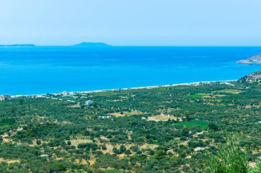 Uzun kumlu Borsh plajı ve yeşil zeytinliklerin tepesinden manzara. Arnavutluk. İyon Denizi. Yaz güneşli mavi manzara.