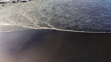 Güneş tarafından aydınlatılan siyah volkanik kumun olduğu bir sahilde sörf dalgaları. Doğal arka plan. Kanarya Adaları, Tenerife, İspanya. Atlantik kıyısı.