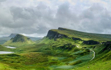 Beautiful,dramatic Scottish, Skye mountain scenery,jagged peaks,winding road and sheer cliffs, along the Quiraing hills walk,green course grass covered in mid summer,in the north east. clipart