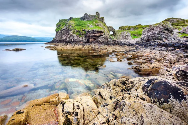 stock image Next to the peaceful waters at low tide,,in mid summer,remains of an acient,historic Scottish castle,overlook,smooth surface of the Loch and many boulders and pebbles in seawater pools.