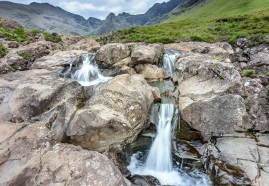 Kara Cuillin Dağları eteklerindeki uzun şelaleler ve kayalık dağ havuzları, popüler turistik yerler, muhteşem Skye manzarası, kayalarla ve yüzme alanlarıyla sarp bir yol..