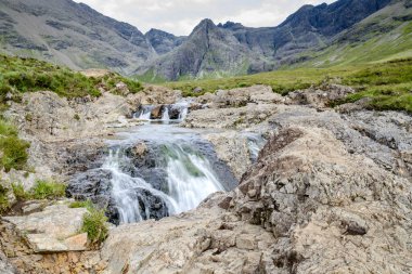 Kara Cuillin Dağları eteklerindeki uzun şelaleler ve kayalık dağ havuzları, popüler turistik yerler, muhteşem Skye manzarası, kayalarla ve yüzme alanlarıyla sarp bir yol..