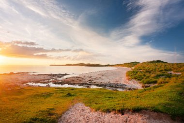 İskoçya 'nın aşırı kuzey batı ucu. Güzel kumlar ve çimenli kum tepeleri üzerinde parlayan dramatik sıcak gün batımı ışığı, ince bulutlar ve yukarıda turuncu gökyüzü, muhteşem İskoç yaz havası..