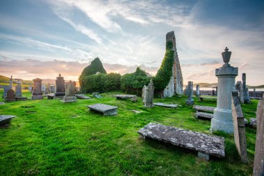 Durness yakınlarındaki büyülü tarihi yer, 8. yüzyıl, önemli Kelt manastırı, antik mezar taşları ve mezarlık, çimlerle kaplı, dramatik günbatımı gökyüzü, Balnakeil Körfezi, alacakaranlıkta ürkütücü atmosfer.