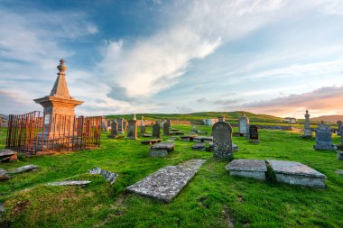 Durness yakınlarındaki büyülü tarihi yer, 8. yüzyıl, önemli Kelt manastırı, antik mezar taşları ve mezarlık, çimlerle kaplı, dramatik günbatımı gökyüzü, Balnakeil Körfezi, alacakaranlıkta ürkütücü atmosfer.