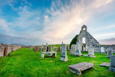 Durness yakınlarındaki büyülü tarihi yer, 8. yüzyıl, önemli Kelt manastırı, antik mezar taşları ve mezarlık, çimlerle kaplı, dramatik günbatımı gökyüzü, Balnakeil Körfezi, alacakaranlıkta ürkütücü atmosfer.