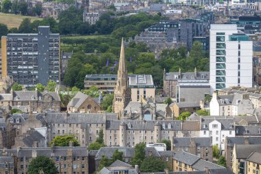 Konut binaları ve bahçelerle çevrili belirgin bir kule. Hava durumu, yeşil ağaçlar ve taretli apartmanlar..