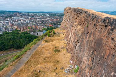 Edinburgh, İskoçya-Ağustos 01-2022: İkonik zirveye tırmanan ziyaretçiler, İskoçya 'nın başkentinde bir yaz gününde Edinburgh' un karşısındaki dev dikey bir uçurumun uçurumunda huşu içinde dururlar..