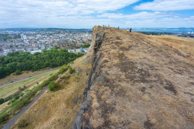 Edinburgh, İskoçya-Ağustos 01-2022: Arthur 'un koltuğuna tırmanan ziyaretçiler, İskoçya' nın başkentinde bir yaz günü, Edinburgh City 'nin karşısındaki yüksek dikey bir uçurumun uçurumunda korku içinde dikiliyorlar..