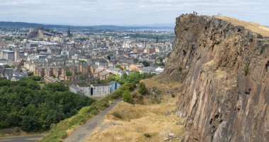 Edinburgh, İskoçya-Ağustos 01-2022: İkonik zirveye tırmanan ziyaretçiler, İskoçya 'nın başkentinde bir yaz gününde Edinburgh' un karşısındaki dev dikey bir uçurumun uçurumunda huşu içinde dururlar..