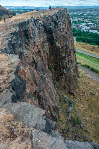 Edinburgh, İskoçya-Ağustos 01-2022: İkonik zirveye tırmanan ziyaretçiler, İskoçya 'nın başkentinde bir yaz gününde Edinburgh' un karşısındaki dev dikey bir uçurumun uçurumunda huşu içinde dururlar..