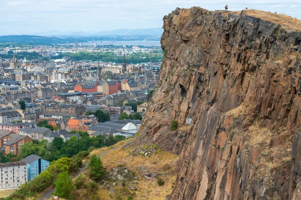 Edinburgh, İskoçya-Ağustos 01-2022: İkonik zirveye tırmanan ziyaretçiler, İskoçya 'nın başkentinde bir yaz gününde Edinburgh' un karşısındaki dev dikey bir uçurumun uçurumunda huşu içinde dururlar..