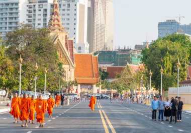 Phnom Penh, Kamboçya-23 Aralık 2023: Geleneksel turuncu cüppeler, keşişler, maske takan birçok kişi, güneşli bir öğleden sonra trafiğe kapalı, geniş bir yolda Kraliyet Sarayı Parkı 'nın önünden geçtiler..