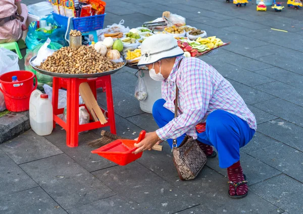 2022年12月23日カンボジア プノンペン 小さな屋台の周りで 夕暮れ時に ダスパンとブラシでナッツや果物の軽食を販売している女性が パン粉とピーナッツの殻をクリアします — ストック写真