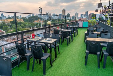 Açılış saatinden önce, müşteriler için Kamboçya başkentinde manzaralı bir yemek masası hazırlandı. Yeşil çimen efekti halısıyla kaplı zemin, Khmer güneşi tapınakların ve uzak binaların arkasında batıyor..