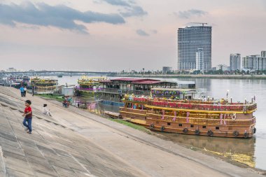 Phnom Penh, Kamboçya-23 Aralık 2022: Alacakaranlıkta, Tonle Sap nehrinin kıyısında, gece ve Mekong nehri boyunca gece gezileri için kullanılan bu canlı ışıklı zanaatın yanından geçtiler..