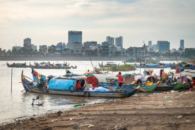 Nehrin batısından çok daha az gelişmiş çamurlu doğu kıyısında bulunan küçük tekneler, suya yansıyan güneş, küçük gemilerin ve uzak şehir binalarının siluetlerini oluşturur..