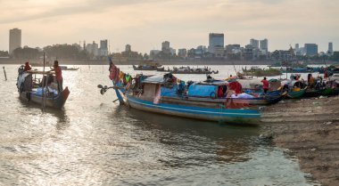 Phnom Penh, Kamboçya-24 Aralık 2022: Kısmen elementlere karşı kaplanmış ve Khmer aileleri tarafından konut olarak kullanılan küçük dar botlar, gün batımında Tonle Sap nehrinin az gelişmiş doğu yakasında yer alır..