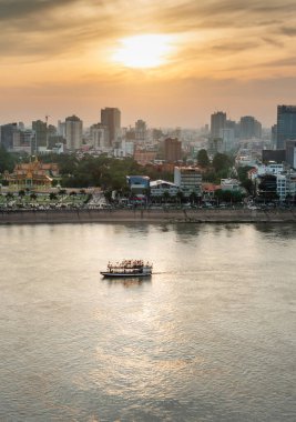 Çatı manzarası, Kamboçya 'nın başkentinin Riverside bölgesine bakıyor. Kraliyet Sarayı üzerinde gün batımı ve yüksek binalar üzerinde küçük bir tekne Mekong Nehri kavşağına doğru sürükleniyor..