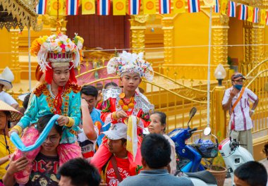 Pai, Mae Hong Son, Tayland-4 Nisan 2023: 7-14 yaşları arasında Budist rahipler olarak atanmak üzere olan çocuklar, kalabalığın kutlamaları sırasında erkeklerin omuzlarında sokaklarda taşınıyor..