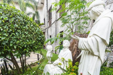 Cebu, Filipinler-17 Ocak 2023: Tarihi Katolik ikonlarının heykelleri ve Cebu 'daki en eski kilisenin yemyeşil çimlerinin ve yemyeşil bitkilerin arasında bir çocuk figürü.