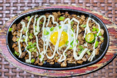 Geleneksel yemek Filipinler 'de yaygın olarak bulunur, doğranmış domuz parçaları ve tavuk ciğeri ile yapılır, doğranmış soğanla süslenir, kızarmış yumurta, limon ve üzeri mayonezle kaplanır..