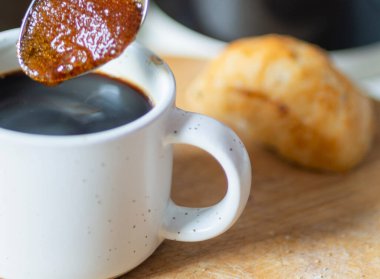 Kahverengi şeker taneleri sıcak kahveyi hazırlar, şerbetli bir dokuya çevirir, taze demlenmiş siyah bir espresso ile karıştırılmadan önce, kahvaltıda sıcak ve tatlı bir şekilde, bir ekmek rulosuyla,.