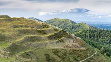 Uzak tepe yürüyüşçüleri Herefordshire Beacon 'ın zirvesinde duruyor, kuzeye, Malvern Hills' in ikonik tepelerine doğru bakıyor, ve Worcestershire Beacon, güneşli yaz havasında, gün batımına doğru..