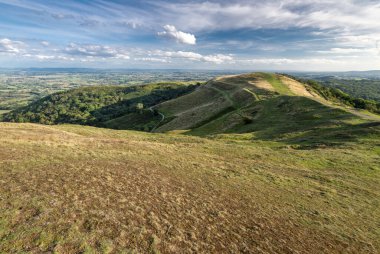 Malvern Hills 'in güney ucu, pürüzsüz yeşil yamaçlar Herefordshire Beacon' ın zirvesinden antik tepenin üzerinden güneşli bir yaz öğleden sonra kırsal Gloucestershire 'a kadar uzanır..