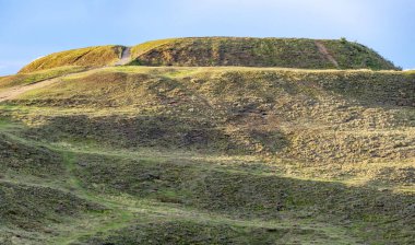 Anonim bir insan figürü, Beacon 'ın güney yakasına giden ana tepe yürüyüş yolundan yükselerek eski Demir Çağ kalesinin zirvesine çıkıyor. Güneşli bir yaz günü öğleden sonra, gün batımına yakın..