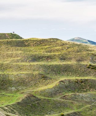 Uzak tepe yürüyüşçüleri Herefordshire Beacon 'ın zirvesinde duruyor, kuzeye, Malvern Hills' in ikonik tepelerine doğru bakıyor, ve Worcestershire Beacon, yaz havasında, gün batımında.